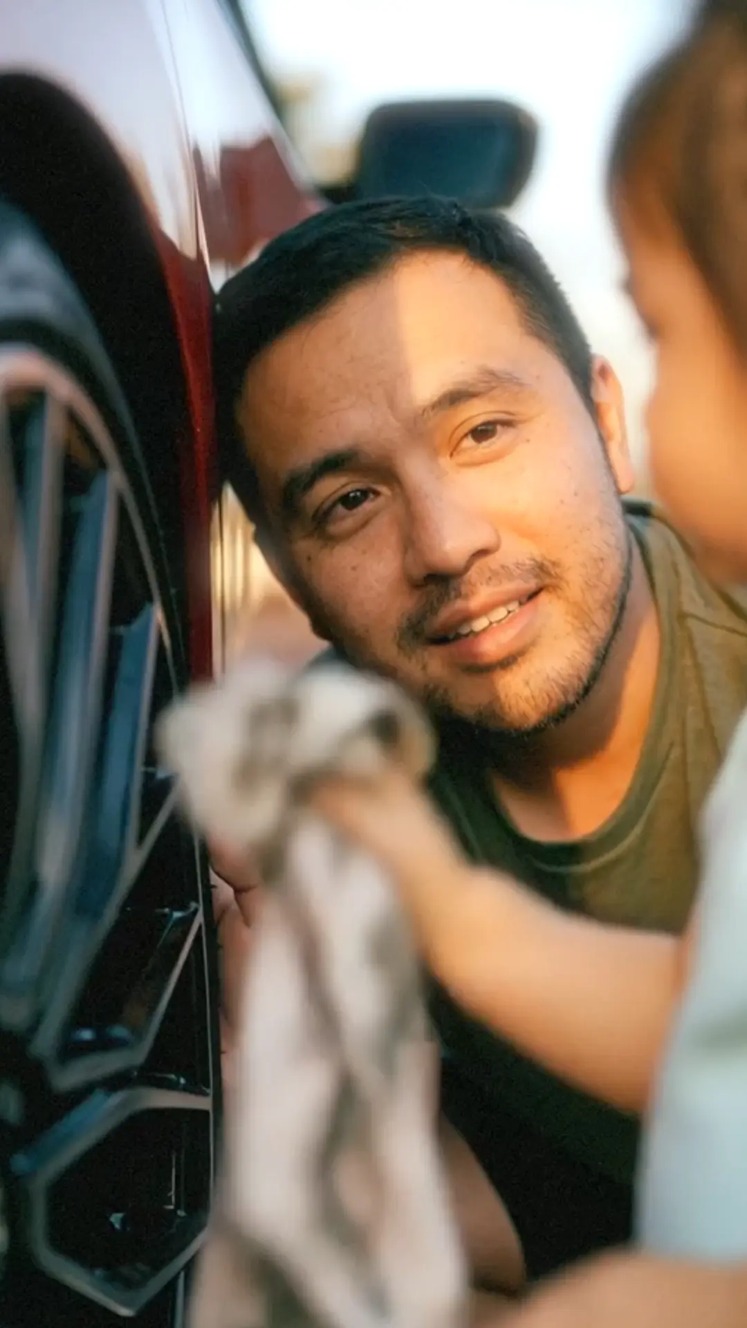 A father and daughter are polishing the aluminum wheels of a red car with a cloth
